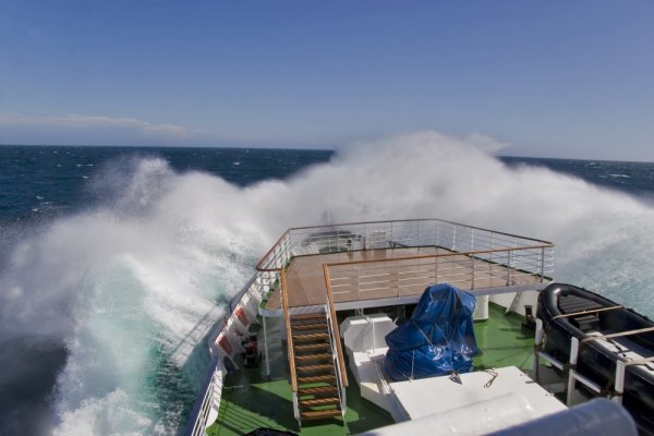 The bow of an expedition cruise ship splashes in rough seas